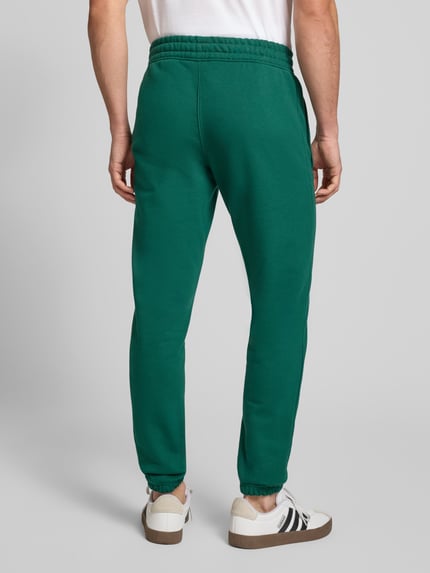 Mężczyzna nosi Sweatpants mit elastischem Bund od adidas Originals, bawełniana mieszanka, luźny krój, kieszenie, widok całej sylwetki z tyłu.