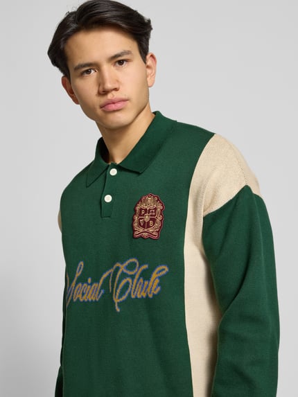 Männermodel trägt Strickpullover mit Polokragen und Label-Patch von PROHIBITED in Grün und Beige aus reiner Baumwolle, Relaxed-Fit, Nahaufnahme Oberkörper.