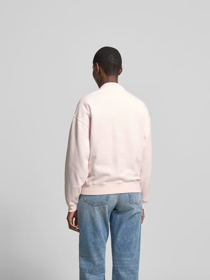 Frauenmodel trägt Regular Fit Sweatshirt mit Logo-Detail von Anine Bing aus reiner Baumwolle in hellem Rosa, elastische Abschlüsse, Rückenlänge bei Größe S 65 cm, Ganzkörperansicht Rückansicht.