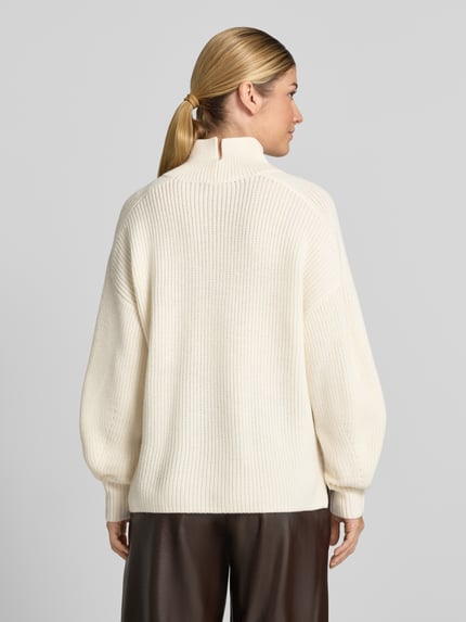 Modelka nosi Strickpullover aus Schurwolle mit Stehkragen od windsor., kremowy kolor, gruby splot, relaxed fit, długość tyłu 59 cm, długość rękawa 57 cm, widok całej sylwetki z tyłu.