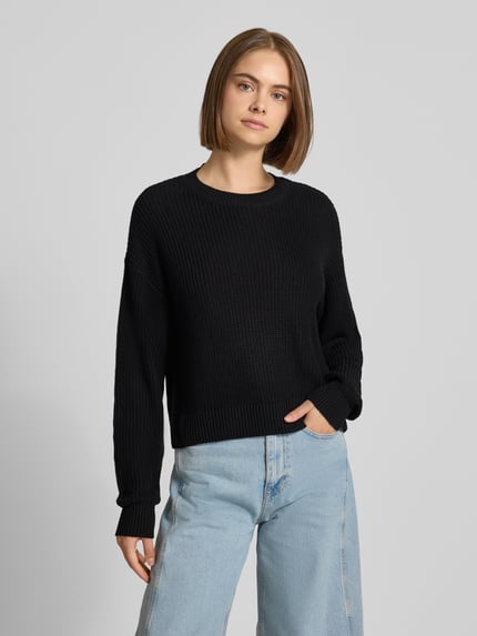 Vrouwenmodel draagt Relaxed Fit Pullover uit katoenmix model 'Maysa' van NOISY MAY, zwart, grofgebreide textuur, ronde hals, voorkant foto, ruglengte 50 cm, mouwlengte 59 cm.