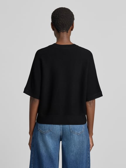 Frauenmodel trägt schwarzen Relaxed Fit Pullover aus Viskose-Mix Modell 'Thamira' von MSCH Copenhagen, Strick-Optik, Ganzkörperansicht Rückansicht.