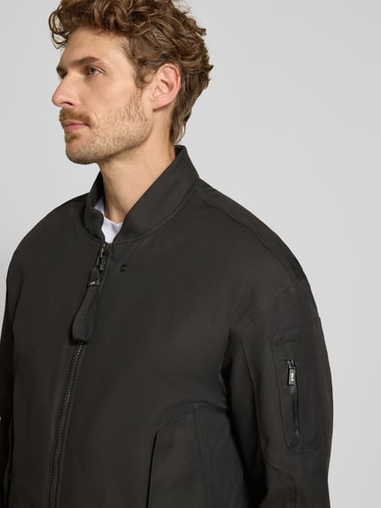 Männermodel trägt Regular Fit Jacke aus Baumwoll-Mix Modell 'Pulse' von g-lab, stójka, kieszeń na rękawie, wpuszczane kieszenie, elastyczne wykończenia, Długość tyłu w rozmiarze M: 70 cm, Szerokość ramion w rozmiarze M: 55 cm, Szerokość klatki piersiowej w rozmiarze M: 50 cm, Długość rękawów w rozmiarze M: 61 cm, kolor ciemny, gładka tekstura, Nahaufnahme górnej części ciała.