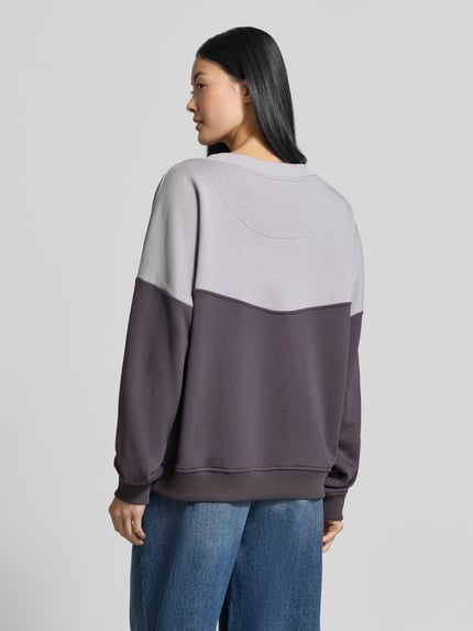 Frauenmodel trägt Oversized Sweatshirt aus reiner Baumwolle von miss goodlife in Grau und Dunkellila mit gerippten Abschlüssen, Ganzkörperansicht Rückansicht.