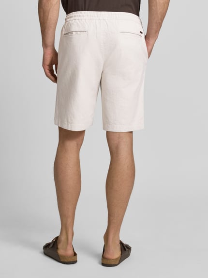 Männermodel trägt Bermudas mit französischen Eingrifftaschen Modell 'COLI' von Fynch-Hatton in Beige, Baumwoll-Mix mit Leinen-Anteil, Loose-Fit, elastischer Bund mit Kordelzug, Gesäßleistentaschen, Innenbeinlänge ca. 22 cm, Ganzkörperansicht Rückansicht.
