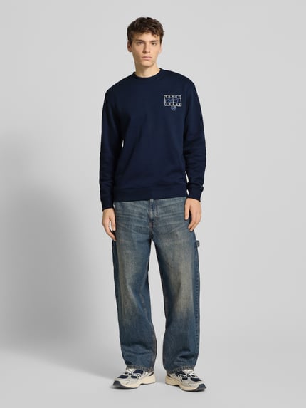 Männermodel trägt Regular Fit Sweatshirt aus reiner Baumwolle von Tommy Jeans, unifarben, Rundhals, langarm, Ganzkörperansicht von vorne.