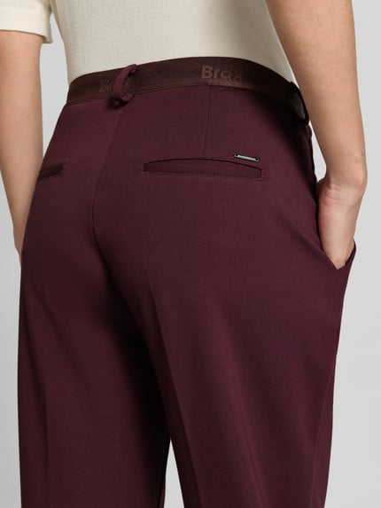 Frauenmodel trägt Regular Fit Chino aus Viskose-Mix Modell 'MARON' von Brax in dunklem Rot, glatte Textur, Damen Schmale Hose, Ganzkörperansicht Rückansicht.
