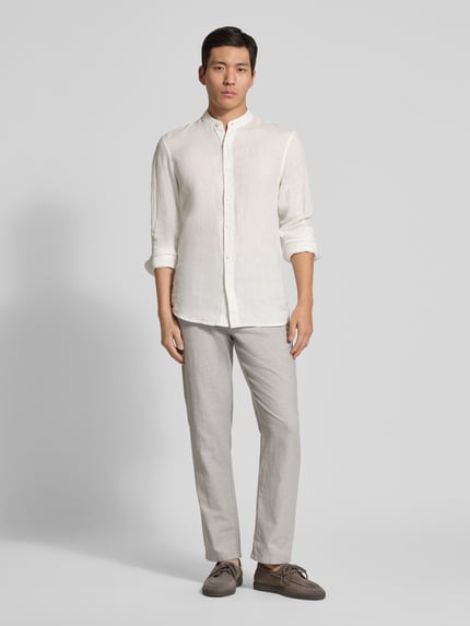 Mannenmodel draagt Regular Fit Leinenhemd mit Stehkragen van Scotch & Soda, zuiver linnen, regular fit, opstaande kraag, knoopsluiting. Volledige lichaamsopname vooraanzicht.