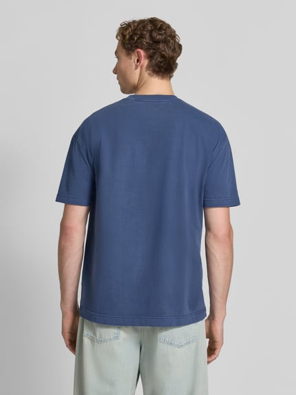 Männermodel trägt T-shirt met ronde hals model 'JOEL' van Samsøe Samsøe, puur katoen, regular fit, ruglengte maat M 72 cm, ganzkörperansicht rugansicht.