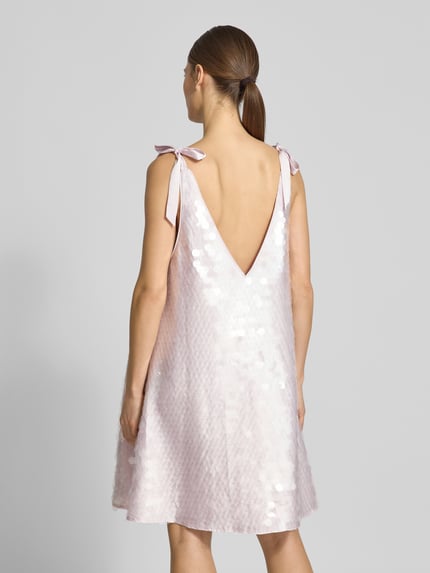 Frauenmodel trägt Relaxed Fit Kleid mit Allover-Paillettenbesatz von Jake*s Cocktail in hellem Rosé, V-Ausschnitt, Zierschleifen, ärmellos, Minilänge, Rückenausschnitt, schimmernde Oberfläche, Ganzkörperansicht Rückansicht.