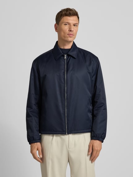 Männermodel draagt Regular Fit Blouson met all-over logomotief, platte kraag, ritssluiting, labelapplicatie uit metaal van BOSS Model 'H-CRESTELL', zij-steekzakken, lange mouwen met elastische mouwboord, tunnelkoord aan de binnenkant van de rompzoom, kleur donkerblauw, structuur glad, look: all-over motief, pasvorm regular fit, voorkant geheel in beeld, Ganzkörperansicht von vorne.