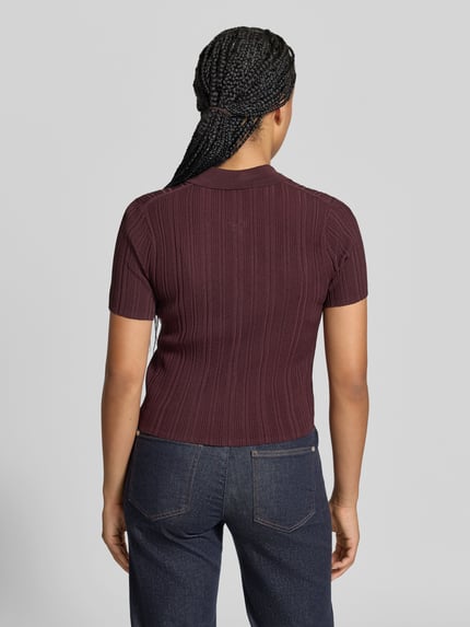 Frauenmodel trägt Poloshirt aus Viskose-Mix von Victoria Beckham in Dunkelrot, Ripp-Optik, Skinny Fit, Kurzarm, Rückenansicht, Ganzkörperansicht Rückansicht.