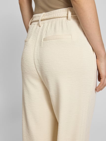 Frauenmodel trägt Wide Fit Stoffhose aus Viskose-Mix Modell 'Lumina' von ICHI, Strukturmuster, Gesäßtasche, Abnehmbare Stoffkordel, cremefarben, Nahaufnahme Rückansicht.