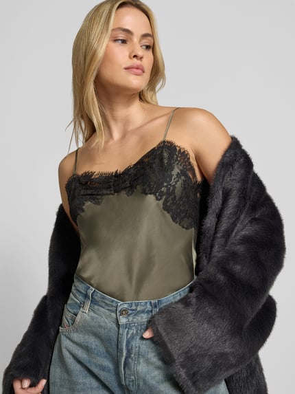 Frauenmodel trägt Top aus reiner Seide von Iro, olivgrün mit schwarzem Spitzenbesatz, Satintextur, Spaghettiträger, Nahaufnahme Oberkörper.