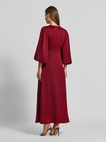 Frauenmodel trägt Cocktailkleid mit Knotendetail und V-Ausschnitt Modell 'THEA' von YAS, A-Linie, Maxikleid, Material-Mix, Ganzkörperansicht Rückansicht.