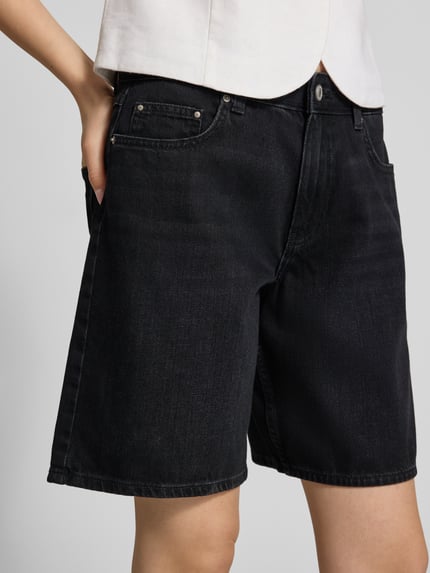 Frauenmodel trägt Regular Fit Jeansshorts aus reiner Baumwolle Modell 'LUMI' von Only in schwarzer Denim-Optik, 5-Pocket-Design, Label-Patch, Bindegürtel, Knopf und verdeckter Reißverschluss, Nahaufnahme Oberkörper.