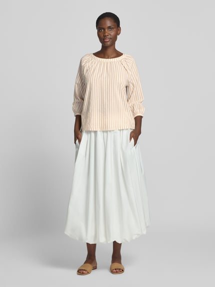 Frauenmodel trägt Loose Fit Kurzarmbluse aus Viskose-Baumwoll-Mix von s.Oliver RED LABEL in Beige mit Streifen, kombiniert mit weißem Rock, Ganzkörperansicht von vorne.