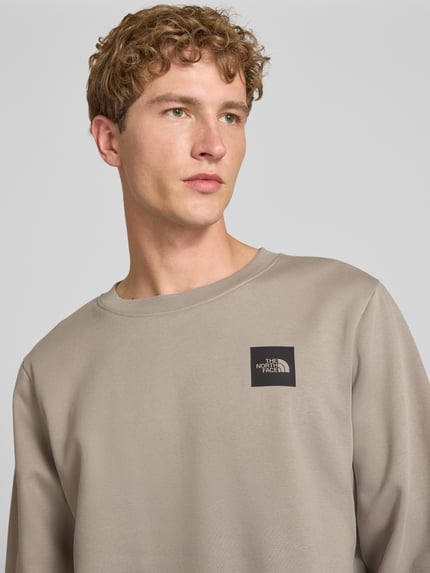 Männermodel trägt Regular Fit Sweatshirt mit Logo-Detail van The North Face in beige katoenmix, logodetail op de borst, Nahaufnahme Oberkörper. Ruglengte maat M: 60 cm, mouwlengte maat M: 70 cm.
