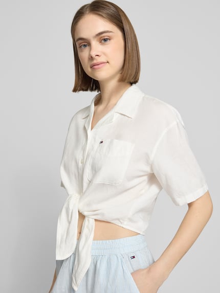 Vrouwenmodel draagt Regular Fit linnen blouse uit linnenmix met strikdetail van Tommy Jeans, effen kleuren, V-hals, korte mouw, gestikt logo, cropped, knoopsluiting, materiaal: linnenmix, nahaufnahme bovenlichaam