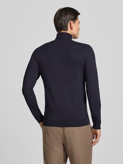 Männermodel trägt Slim Fit Rollkragenpullover aus Viskose-Mix mit Rippbündchen von MCNEAL in Dunkelblau, Ganzkörperansicht Rückansicht. Rückenlänge und Ärmellänge bei Größe M, langärmlig, überschnittene Schultern, Rollkragen, strukturierte Textur, feinmaschig.