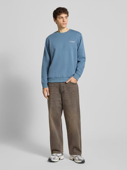 Männermodel trägt Sweatshirt mit Label-Print von Jack & Jones in Blau, Baumwoll-Mix, lockerer Schnitt, gerippte Abschlüsse, Ganzkörperansicht von vorne.