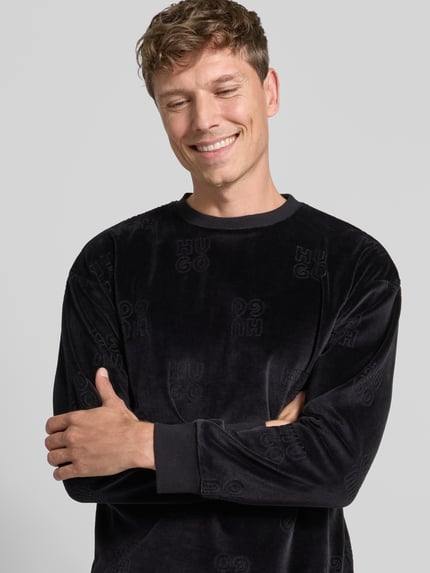 Männermodel trägt Sweatshirt mit Samtstruktur von HUGO in Schwarz mit Allover-Struktur und Rundhalsausschnitt, Nahaufnahme Oberkörper.