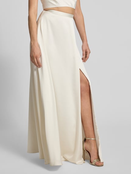 Frauenmodel trägt Relaxed Fit Abendkleid mit Gehschlitz von Jake*s Cocktail in cremefarbener Satin-Optik, Detailaufnahme, Gehschlitz sichtbar.