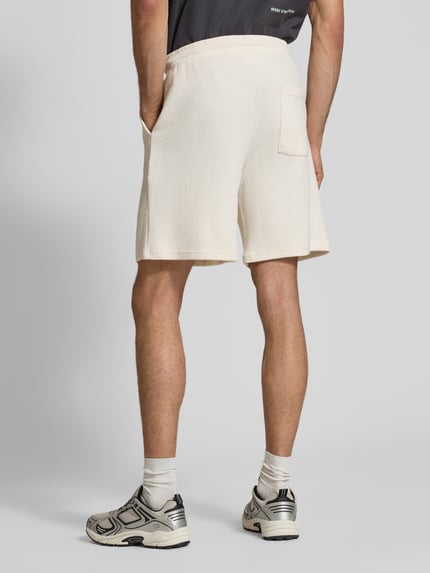 Männermodel trägt Shorts aus Baumwoll-Mix mit Strukturmuster Modell 'KNOX' von Redefined Rebel in Creme mit elastischem Bund und Tunnelzug, Ganzkörperansicht Rückansicht.