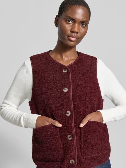 Frauenmodel trägt Fleeceweste mit aufgesetzten Taschen Modell 'ADA' von VILA in Bordeaux, Teddyfelltextur, Regular Fit, Knopfleiste, Nahaufnahme Oberkörper, Damen Fleeceweste von VILA