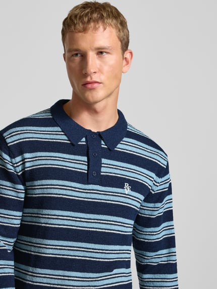 Mężczyznamodel nosi Sweter z dzianiny z imitacją bouclé w wzór w paski, kołnierzyk polo, listwa guzikowa, wyhaftowane logo od REVIEW, krój regular fit, zbliżenie na górną część ciała.