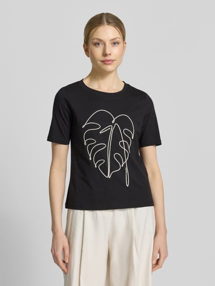 Kobiece model nosi T-Shirt mit Motiv-Stitching od Christian Berg Woman Selection z bawełny, krój regular fit, okrągły dekolt, długość tyłu 54 cm, czarny z białym wyhaftowanym motywem liścia, widok całej sylwetki z przodu.