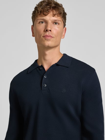 Männermodel trägt Poloshirt mit Logo-Stitching von MARC O'POLO in Dunkelblau, strukturierte Piqué-Optik, Nahaufnahme Oberkörper.