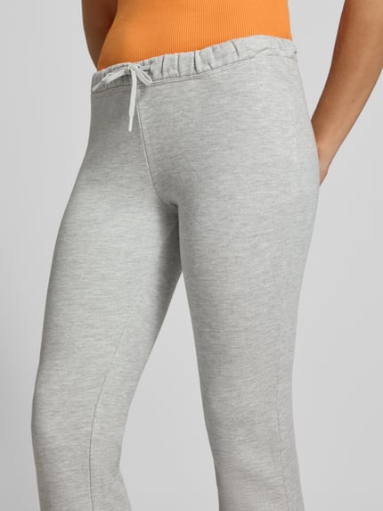 Frauenmodel trägt Flared Sweatpants aus reiner Baumwolle von REVIEW in Hellgrau, elastischer Bund, seitliche Taschen, Nahaufnahme Rückansicht.