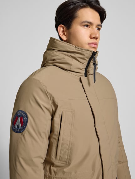 Männermodel draagt Parka met capuchon van Superdry in beige, materiaalmix met stretch, labeldetail, regular fit, nahaufnahme bovenlichaam.
