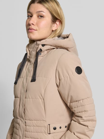 Frauenmodel trägt Jacke mit Kapuze und Label-Patch von G.I.G.A. DX in Beige mit seitlichen Reißverschlusstaschen, Nahaufnahme Oberkörper. Material-Mix mit Baumwoll-Anteil, gerader Schnitt, gestrickte Ärmelabschlüsse, Label-Patch am Arm, Reiß- und Klettverschluss.