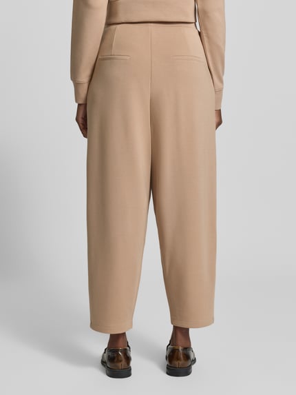 Frauenmodel trägt Barrel Fit Sweatpants mit elastischem Bund von Christian Berg Woman, beigefarbener Material-Mix mit Bundfalten, Ganzkörperansicht Rückansicht.