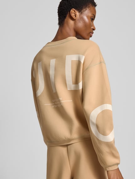 Frauenmodel trägt Sweatshirt mit Rundhalsausschnitt Modell 'Gunda' von GUIDO MARIA KRETSCHMER WOMAN in Beige mit großem Print, Baumwoll-Mix, Relaxed Fit, Ganzkörperansicht Rückansicht.
