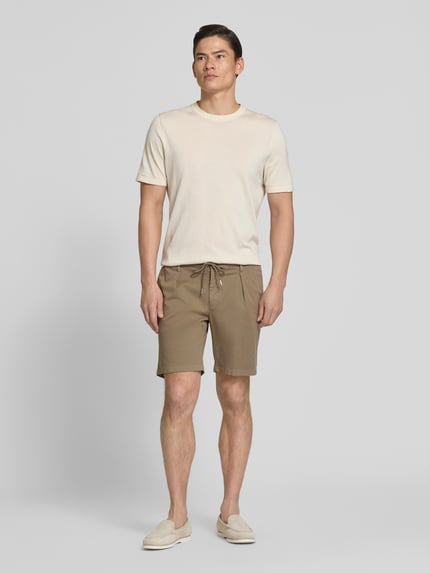 Männermodel trägt Straight Fit Shorts mit Bundfalten von Profuomo in Beige, elastischer Bund, Eingrifftaschen, Ganzkörperansicht von vorne.