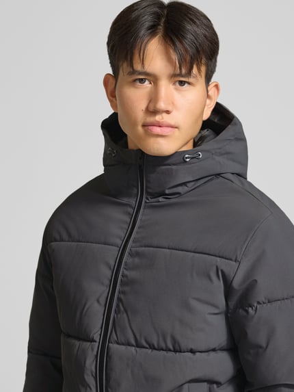 Männermodel trägt Steppjacke mit Kapuze Modell 'GALAXY' von JACK & JONES, schwarze Farbe, glatte Struktur, Nahaufnahme Oberkörper. Regular Fit, Reißverschluss, Eingrifftaschen, Kapuze mit Tunnelzug, Rückenlänge 70 cm, Schulterbreite 49 cm, Brustweite 58 cm, Ärmellänge 69 cm.