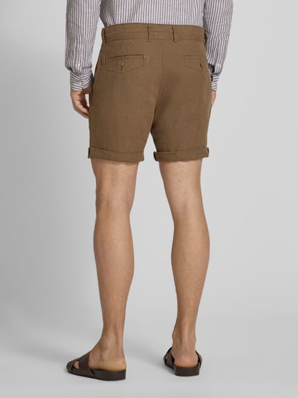 Männermodel trägt Leinenshorts mit Bindegürtel und Gesäßtaschen von MCNEAL in Braun mit Aufschlag und Label-Stitching, Ganzkörperansicht Rückansicht. Reines Leinen, Straight Fit, Knopf-Reißverschluss, Bundweite 45 cm, Innenbeinlänge 16 cm.