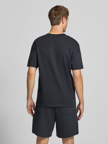 Männermodel trägt schwarzes T-Shirt mit Label-Stitching Modell 'ESSENTIALS' von New Balance, reine Baumwolle, Rückansicht, ganzkörper.