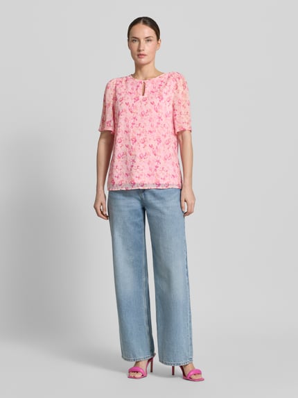 Modelka kobieca ma na sobie Blusenshirt mit Schlüsselloch-Ausschnitt Modell 'EMMA' od Vila, krój regular fit, wzór allover, różowe i jasnoniebieskie kolory, długość tyłu w rozmiarze 36: 60 cm, długość rękawa w rozmiarze 36: 29 cm, pełny widok z przodu.