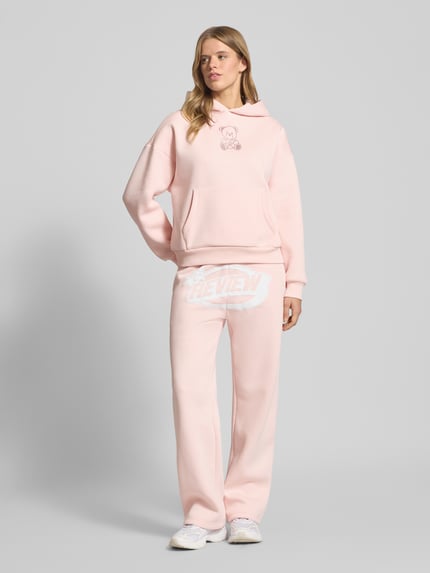 Frauenmodel trägt Hoodie mit Kapuze von Review in zartem Rosa, Ziersteinbesatz, Känguru-Tasche, Baumwoll-Mix, lockerer Schnitt, Ganzkörperansicht von vorne.
