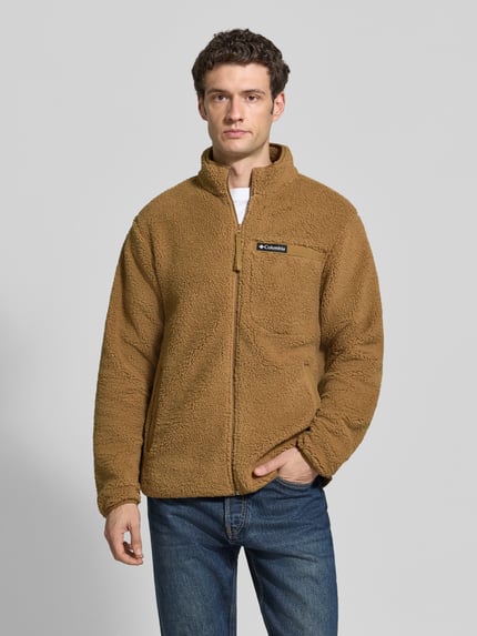 Männermodel trägt Regular Fit Fleecejacke mit Logo-Patch von Columbia in Braun, sichtbar Brusttasche, Stehkragen, Ganzkörperansicht von vorne.
