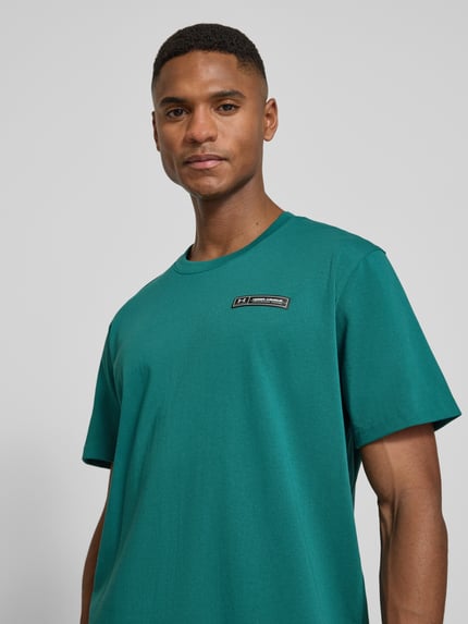 Męski model nosi Regular Fit T-Shirt mit Logo-Applikation od Under Armour, bawełniany miks, okrągły dekolt, krój regular fit, długość tyłu w rozmiarze M: 73 cm, zbliżenie na górną część ciała z przodu