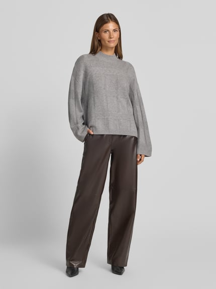 Frauenmodel trägt Oversized Wollpullover mit Kaschmir-Anteil von Emporio Armani in Grau mit Stehkragen, Strukturmuster und gerippten Abschlüssen, Schurwoll-Kaschmir-Mix, kombiniert mit weiter brauner Hose, Ganzkörperansicht von vorne.