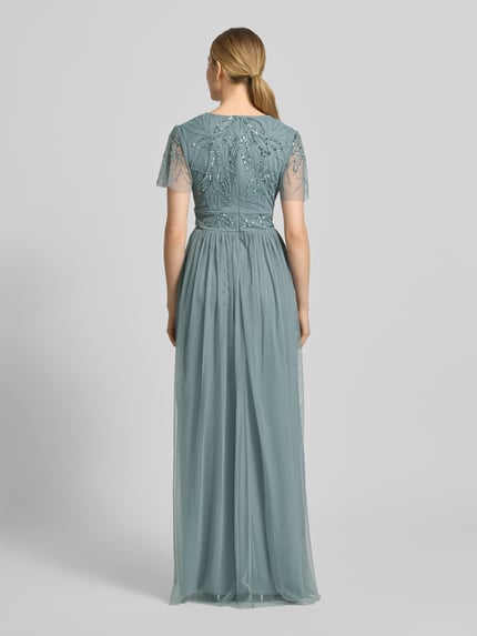 Modelka kobieca ma na sobie sukienkę wieczorową 'Abendkleid mit Ziersteinbesatz' od Christian Berg Cocktail, linia a, długa sukienka, dekolt w serek, marszczenia, zamek błyskawiczny z tyłu, obszycie ozdobnymi kamieniami, długość tyłu w rozmiarze 36: 140 cm, szerokość w rozmiarze 36: 38 cm, długość rękawów w rozmiarze 36: 21 cm, widok całej sylwetki od tyłu.