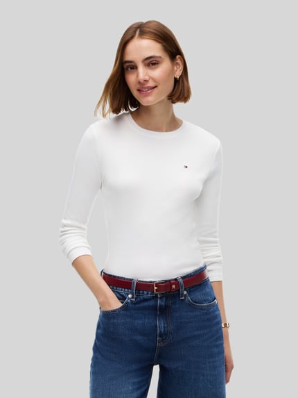 Frauenmodel trägt Slim Fit Langarmshirt aus reiner Baumwolle von Tommy Hilfiger in Weiß, kombiniert mit blauen Jeans, Nahaufnahme Oberkörper. Damen Langarmshirt von Tommy Hilfiger.