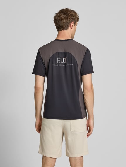 Mężczyznamodel nosi T-Shirt mit Logo Modell 'DIVISION' od HALO, czarny i szary, materiał z domieszką stretchu, krój regular fit, logo na plecach, długość tyłu w rozmiarze M: 69 cm, widok całej sylwetki od tyłu.
