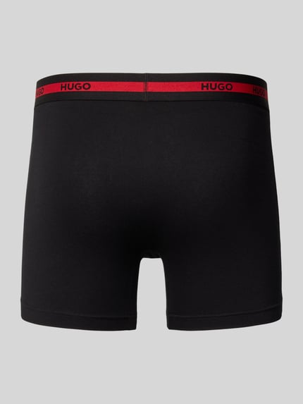 Männermodel trägt Boxershorts mit elastischem Logo-Bund im 3er-Pack von HUGO, Unifarbenes-Design, Baumwoll-Elasthan-Mix, Ganzkörperansicht Rückansicht.
